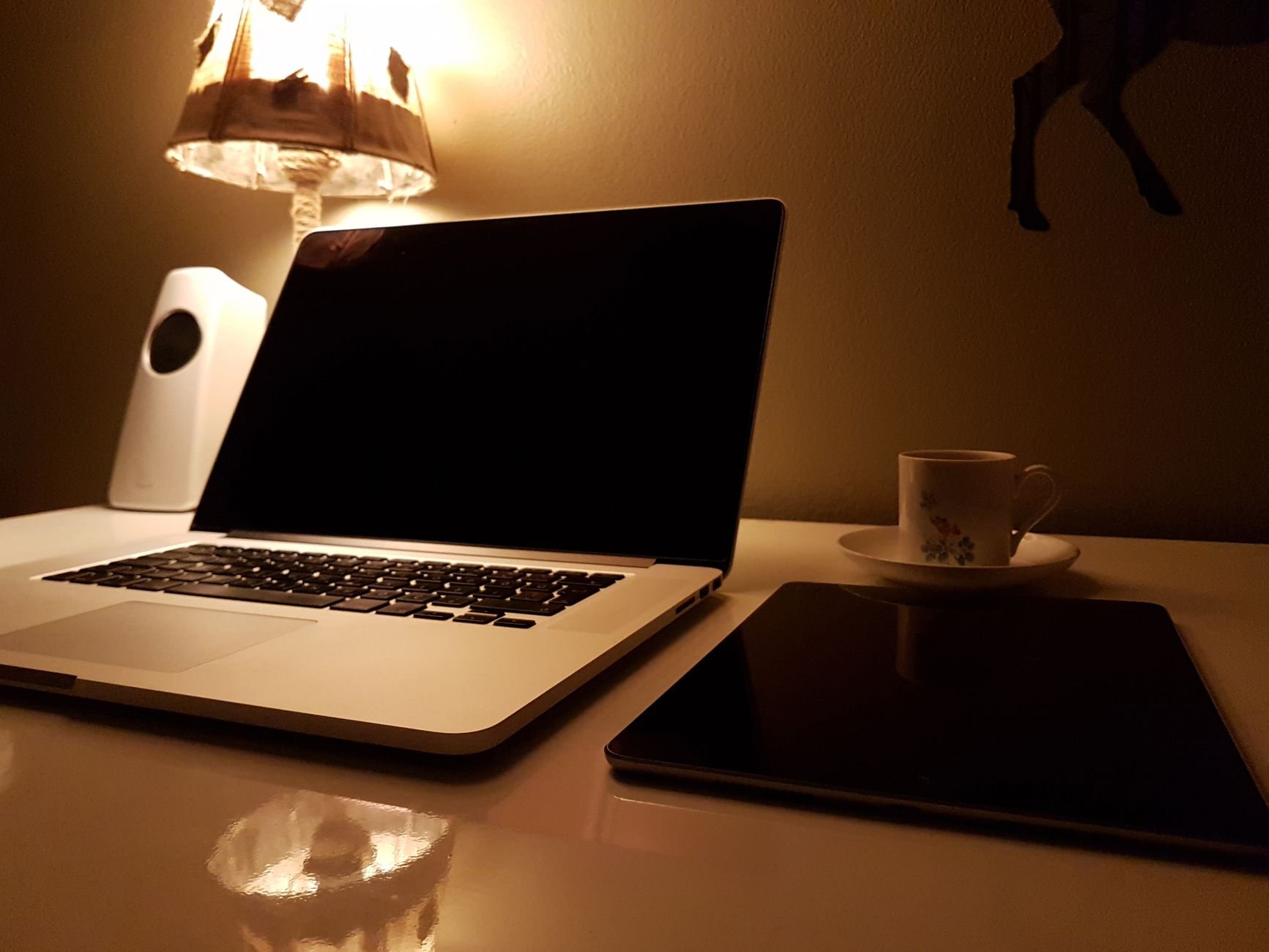 A warmly lit desk featuring a laptop, tablet, and a cup of coffee, creating a cozy late-night work vibe.